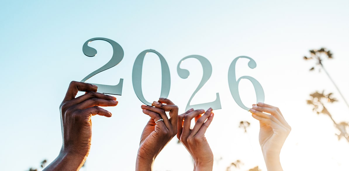 Manos de personas de distintas etnias alzando recortes del número 2026 hacia un cielo claro, simbolizando el inicio de un nuevo año y un compromiso compartido de esperanza y cuidado.