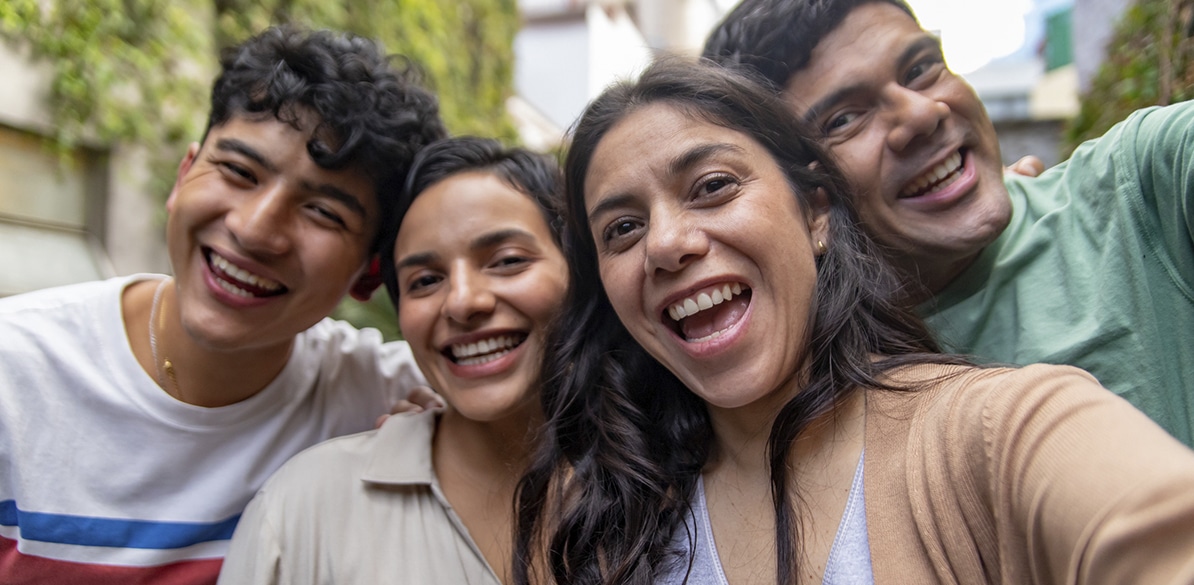 Cuatro jóvenes sonríen mientras se hacen un selfie al aire libre.