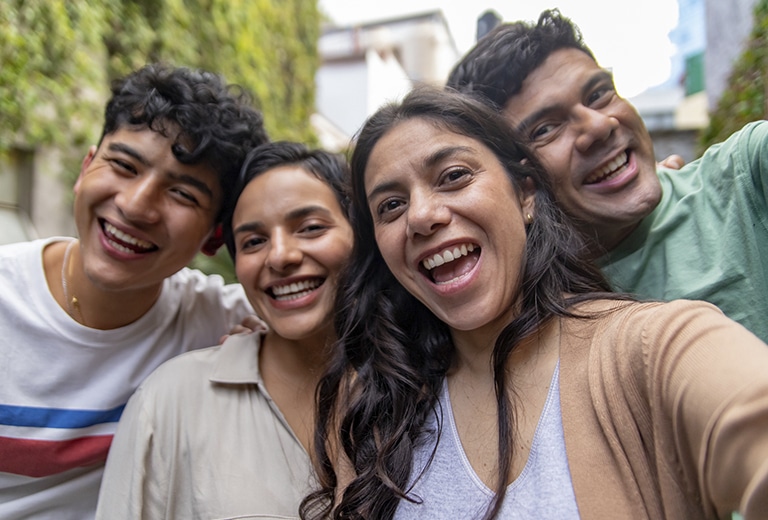 Cuatro jóvenes sonríen mientras se hacen un selfie al aire libre.