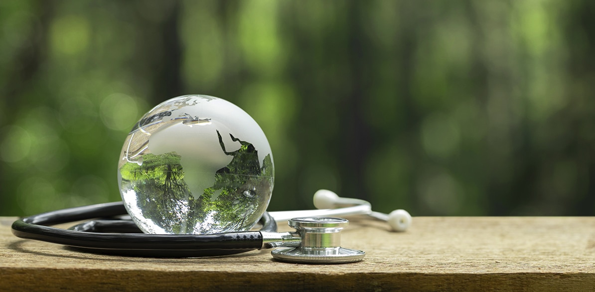 Esfera de cristal sobre una superficie de madera junto a un estetoscopio, con un fondo desenfocado en tonos verdes que evoca naturaleza, salud, bienestar y prevención.
