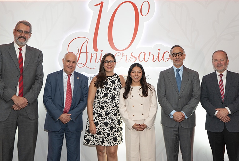 En la imagen se observa a un grupo diverso de personas, probablemente de una organización o evento corporativo. El ambiente parece ser formal y festivo, lo que sugiere que la ocasión es importante. El fondo con el texto "10° Aniversario" resalta el motivo de la celebración. Los participantes lucen trajes formales y se muestran sonrientes, lo que indica una atmósfera positiva y de celebración.