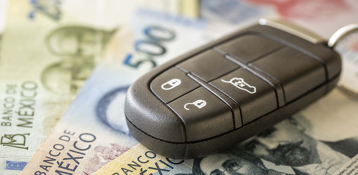 Llave electrónica de automóvil colocada sobre billetes mexicanos de 500 pesos, representando el coste económico de los incidentes viales y la importancia del seguro de auto para la protección financiera.