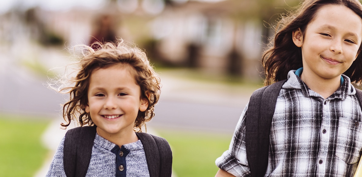 La vuelta al cole Dos niños con mochilas caminando juntos hacia el colegio.