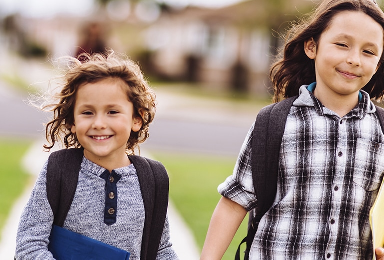 Dos niños con mochilas caminando juntos hacia el colegio.