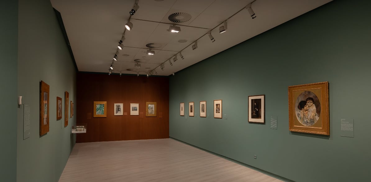 Sala de museo con paredes verdes y marrones, varias obras enmarcadas expuestas a ambos lados, iluminación de galería y un cuadro destacado en primer plano.