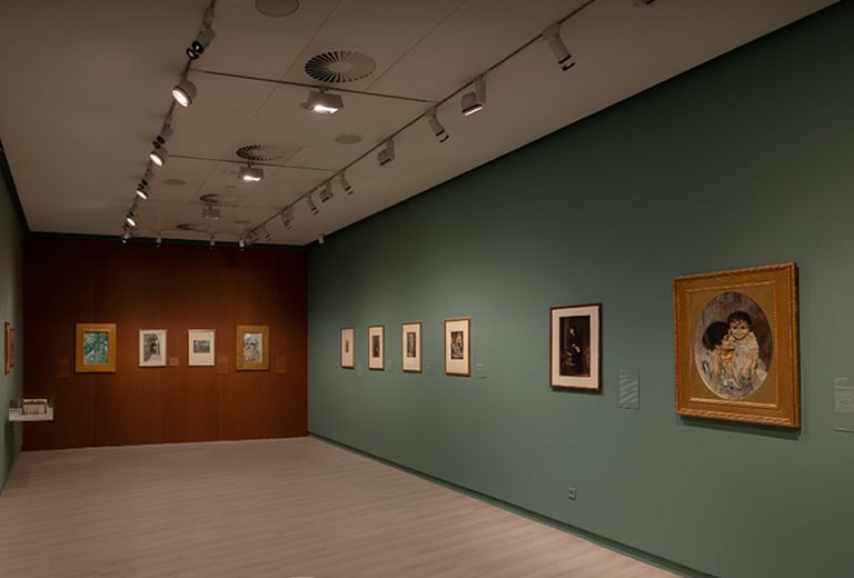 Sala de museo con paredes verdes y marrones, varias obras enmarcadas expuestas a ambos lados, iluminación de galería y un cuadro destacado en primer plano.